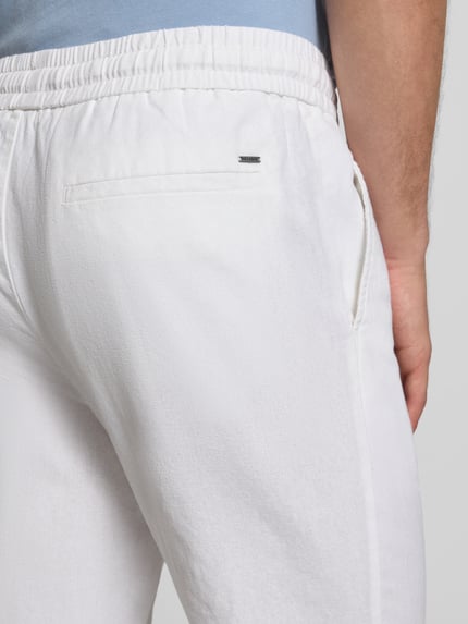 Mężczyzna nosi Tapered Leinenhose aus Baumwoll-Leinen-Mix Modell 'LINUS' von Only & Sons, jasny melanż, kieszenie, detal tyłu, zbliżenie biodra.