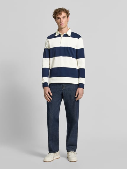 Männermodel trägt Poloshirt aus reiner Baumwolle von Christian Berg Men mit breiten blauen und weißen Streifen, lockere Passform, Ganzkörperansicht von vorne.