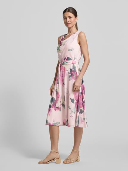 Vrouwenmodel draagt knielange cocktailjurk met strikceintuur van Vera Mont in roze chiffon, getailleerd model, cascadehals, ruglengte maat 36 104 cm, borstwijdte maat 36 40 cm, geheelvooraanzicht