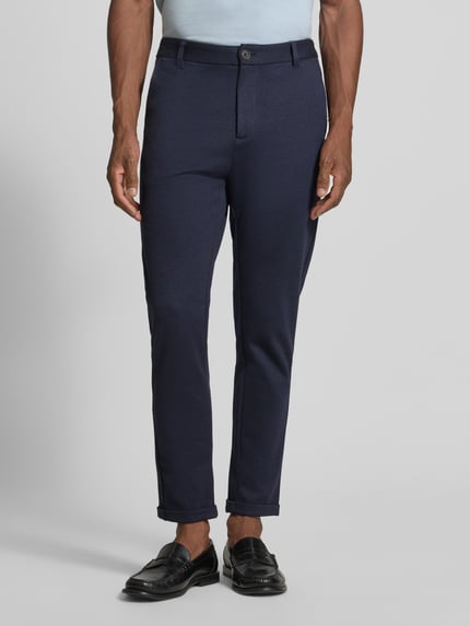 Männermodel trägt Slim Fit Stoffhose mit umgeschlagenen Hosenbeinen von Lindbergh, dunkelblau, Strukturstoff, elastischer Material-Mix, Nahaufnahme Oberkörper, Kontext: Herren Stoffhose von Lindbergh, Viskose-Anteil, Gürtelschlaufen, Bundweite Größe M 43 cm, Innenbeinlänge 73 cm.