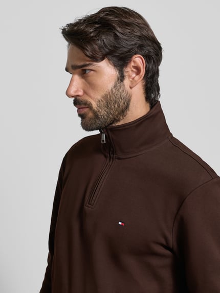 Männermodel trägt Regular Fit Troyer aus Baumwoll-Mix von Tommy Hilfiger, unifarben braun, Label Stitching, Nahaufnahme Oberkörper.