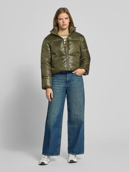 Frauenmodel trägt Puffer Jacket mit glänzender Optik von PIECES in Olivgrün, unifarben, cropped, mit Teilungsnähten und Reißverschluss, Ganzkörperansicht von vorne.
