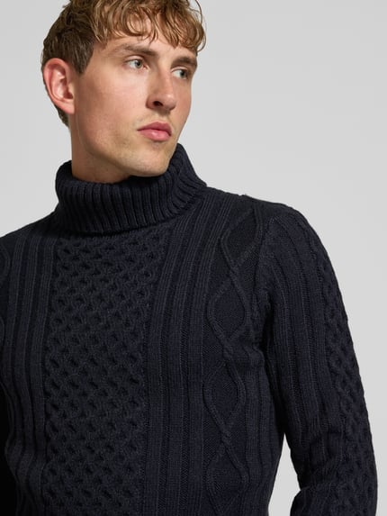 Männermodel trägt Rollkragenpullover mit Zopfmuster von Superdry, dunkelblau, strukturierte Stricktextur, Material-Mix, Nahaufnahme Oberkörper.