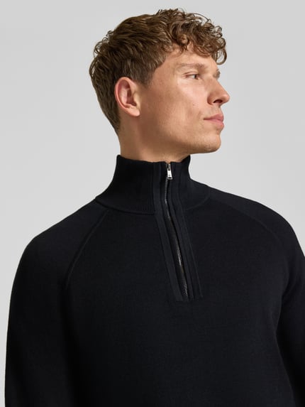 Männermodel trägt Pullover aus Wolle mit Troyerkragen Modell 'H-Fabio' von BOSS in unifarbener Strickoptik mit Struktur, Nahaufnahme Oberkörper.