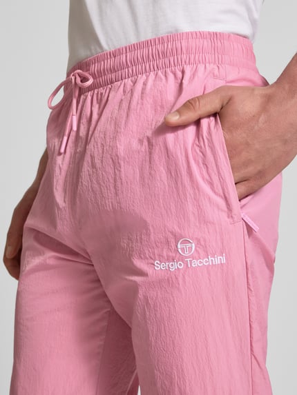 Männermodel trägt Straight Fit Stoffhose mit Logo-Stitching Modell 'Nayla' von SERGIO TACCHINI in Rosa, Nahaufnahme Oberkörper, Herren, elastischer Bund mit Tunnelzug, elastische Beinabschlüsse, Innenbeinlänge bei Größe M 77 cm.