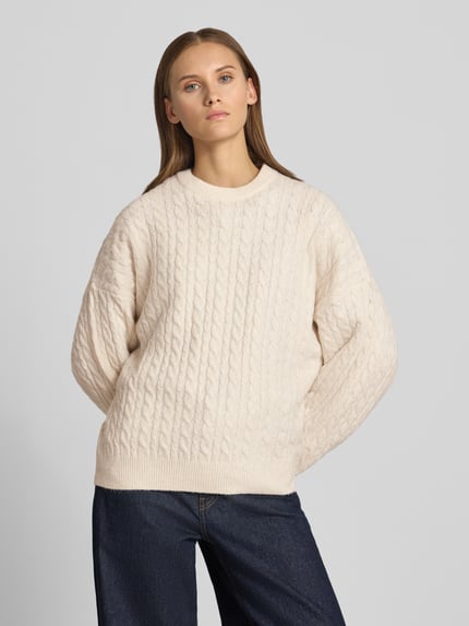 Frauenmodel trägt Oversized Fit Strickpullover mit Zopfmuster von REVIEW, beige Farbe, elastischer Material-Mix, Ganzkörperansicht von vorne.