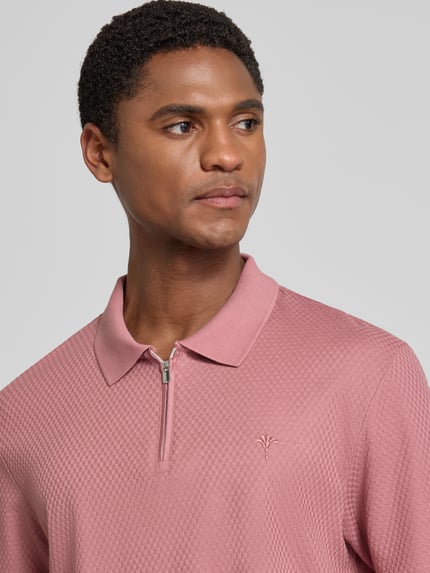 Männermodel trägt Regular Fit Poloshirt mit Strukturmuster Modell 'Tibaris' von JOOP! COLLECTION in Rosa, Nahaufnahme Oberkörper, Label-Stitching, Polokragen, Reißverschluss, Rückenlänge 70 cm bei Größe M.