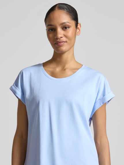 Kobiece modelka nosi t-shirt z okrągłym dekoltem od monari, czysta bawełna, krój regular fit, rękawy z zakładką, długość tyłu 59 cm przy rozmiarze 36, jasnoniebieski kolor, gładka faktura, zbliżenie na górną część ciała, ujęcie z przodu.