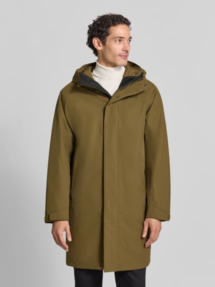 Męski model nosi Regular Fit Parka mit Logo Modell 'Treeline HIPE' von Peak Performance, kolor oliwkowy, Kaptur, zamek błyskawiczny kryty, Długość tyłu w rozmiarze M: 100 cm, szerokość ramion w rozmiarze M: 50 cm, szerokość klatki piersiowej w rozmiarze M: 57 cm, długość rękawów w rozmiarze M: 62 cm, widok całej sylwetki z przodu.