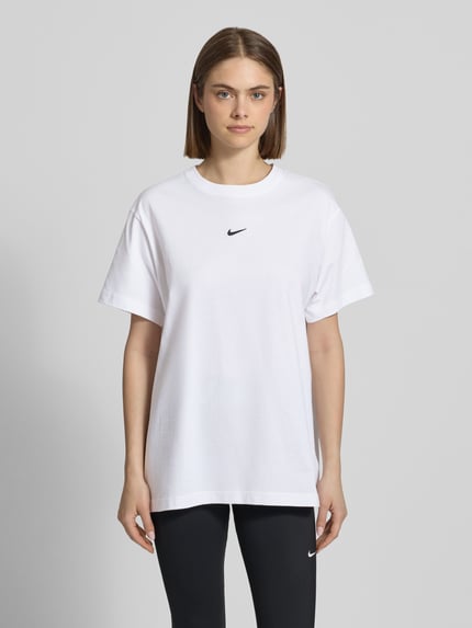 Frauenmodel trägt T-Shirt mit Logo und Rundhalsausschnitt von Nike in Weiß, Reine Baumwolle, Relaxed-Fit, Rückenlänge 69 cm, Ganzkörperansicht von vorne.
