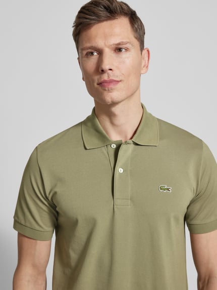 Männermodel trägt Regular Fit Poloshirt aus Baumwoll-Mix von Lacoste in Olivgrün, unifarben, Piqué-Struktur, Nahaufnahme Oberkörper.