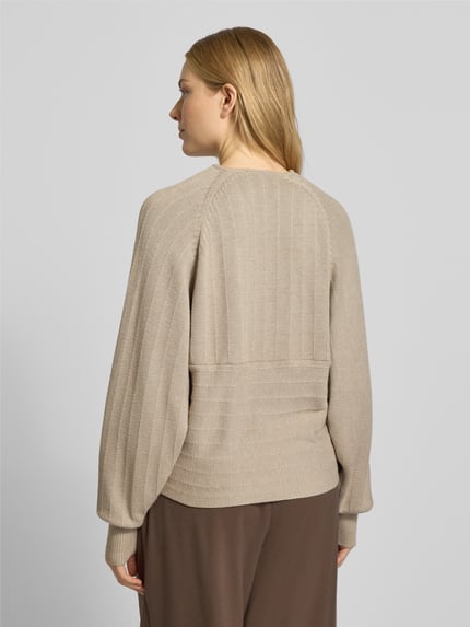 Vrouwenmodel draagt gebreide pullover in wikkellook model 'Zine Rachelle' van MSCH Copenhagen, viscosemix, relaxed fit, ruglengte 57 cm, mouwlengte 50 cm, kleur beige, structuur met verticale en horizontale lijnen, rugaanzicht, Ganzkörperansicht Rückansicht.
