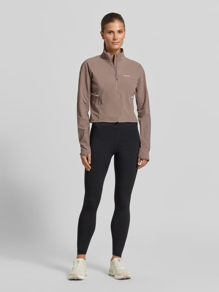 Frauenmodel trägt Cropped Pullover für intensive Anstrengungen und Beschleunigung von Salomon aus Material-Mix mit Stretch-Anteil, Logo, Stehkragen und Reißverschluss, Rückenlänge bei Größe S: 47 cm, Ganzkörperansicht von vorne.