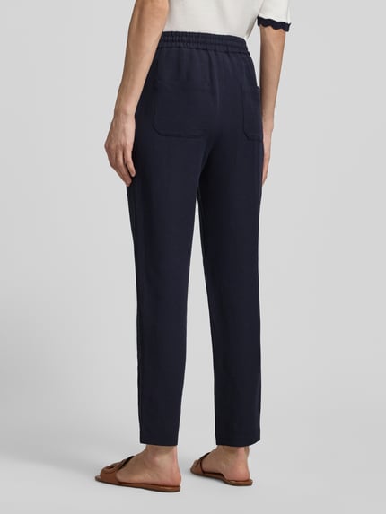 Kobiece modelka nosi Straight Fit Stoffhose aus Viskose-Mix mit Leinen-Anteil von Marc Cain, granat, materiał stylizowany na len, wpuszczane kieszenie, elastyczny pas z tunelem, szerokość w rozmiarze 36: 37 cm, długość wewnętrzna nogawki 66 cm, Ganzkörperansicht Rückansicht.
