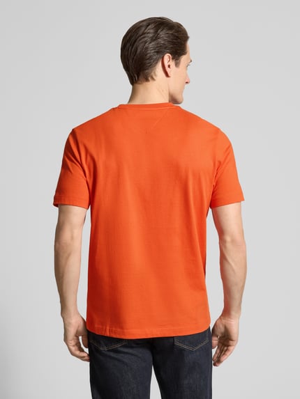 Männermodel trägt Regular Fit T-Shirt aus reiner Baumwolle von Tommy Hilfiger in Orange, unifarben, Kurzarm, Ganzkörperansicht Rückansicht.