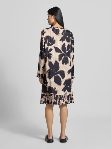 Frauenmodel trägt figurnah geschnittenes Freizeitkleid aus reiner Viskose Modell 'NOS JULI' von Betty Barclay mit großflächigem Blumenmuster in Beige und Dunkelblau, Ganzkörperansicht Rückansicht, Damen Freizeitkleid von Betty Barclay.