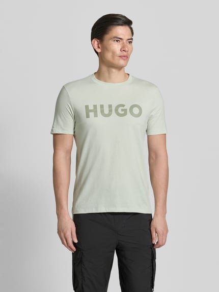 Męski model nosi Relaxed Fit T-Shirt aus reiner Baumwolle Modell 'DULIVIO' von HUGO, kolor jednolity, jersey, nadruk z logo, krój relaxed fit, t-shirt z krótkim rękawem, widok całej sylwetki z przodu.
