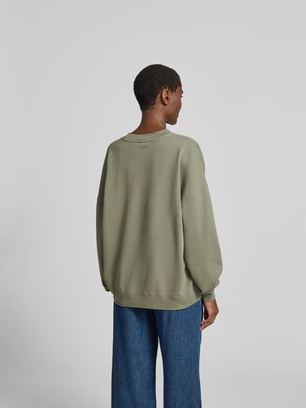 Frauenmodel trägt Relaxed Fit T-Shirt mit Logo-Print von Anine Bing aus reiner Baumwolle, olivegrün, Rundhalsausschnitt, eingefasste Ärmelabschlüsse, Rückenlänge bei Größe S 60 cm, Ganzkörperansicht Rückansicht.