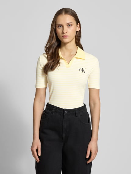 Vrouwenmodel draagt Slim Fit Poloshirt met Label-Stitching van Calvin Klein Jeans in geel met zachte ribtextuur, katoen-elastaanmix, V-hals, vooraanzicht bovenlichaam.
