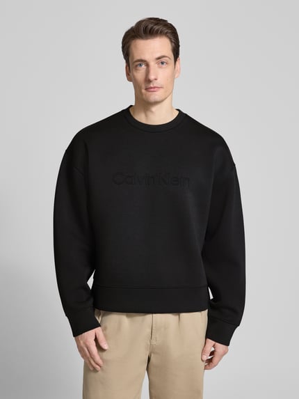 Männermodel trägt schwarzes Sweatshirt mit Rundhalsausschnitt und Logo von CK Calvin Klein im Material-Mix mit Viskose-Anteil, Regular-Fit, Nahaufnahme Oberkörper.