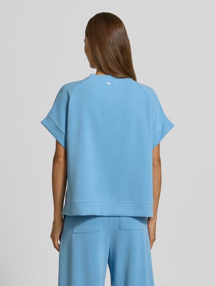 Vrouwenmodel draagt t-shirt met elastische boordjes van Rich & Royal in lichtblauw, modalmix met stretch, relaxed fit, ronde hals, volledig zicht van achteren.