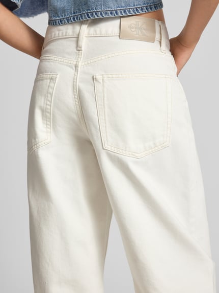 Kobiece model nosi Barrel Jeans im 5-Pocket-Design mit Label-Detail od Calvin Klein Jeans z bawełny, krój relaxed fit, detal z logo, kremowa faktura, długość wewnętrzna nogawki 77 cm w rozmiarze 27/32, szerokość w rozmiarze 27/32: 39 cm, widok tyłu w zbliżeniu.