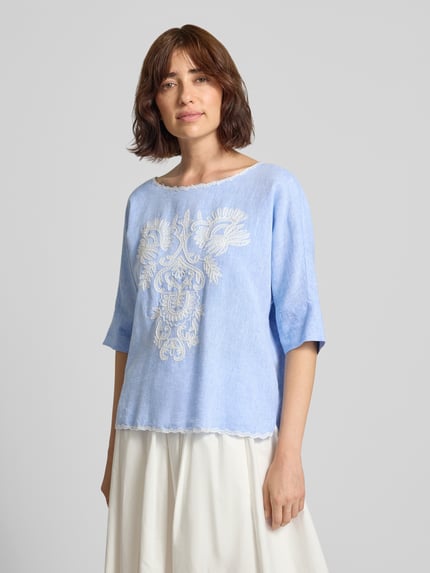 Modelka nosi Blusenshirt mit Leinen-Anteil und Motiv-Stitching von Christian Berg Woman, Mieszanka wiskozy i lnu, krój loose fit, dekolt w łódkę z kontrastową lamówką, wyhaftowany motyw, jasnoniebieski odcień, Długość tyłu w rozmiarze 36: 55 cm, Długość rękawów w rozmiarze 36: 34 cm, całkowity widok z przodu.
