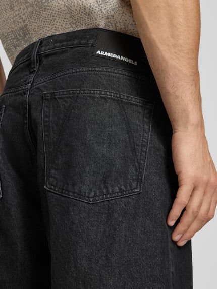 Mężczyzna nosi Loose Fit Jeansshorts aus Baumwoll-Mix Modell 'BAGGY' od Armedangels, czarny denim z łatką z logo, detaliczne ujęcie tylnej części.
