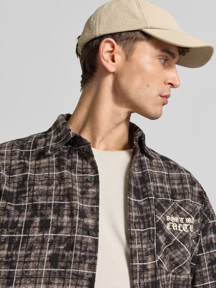 Männermodel trägt Regular Fit Freizeithemd mit Label-Print von Don't Waste Culture, braun-schwarz kariert, reine Baumwolle, Nahaufnahme Oberkörper.