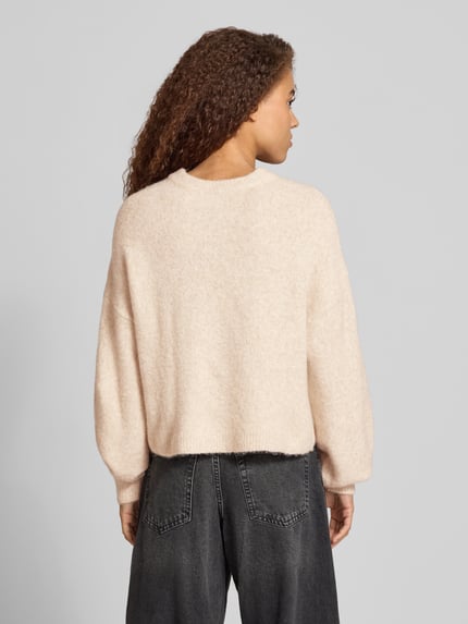 Frauenmodel trägt Relaxed Fit Strickpullover mit Rundhalsausschnitt Modell 'VIXEN' von NOISY MAY®, beige, weiche Textur, Ganzkörperansicht Rückansicht. Material-Mix mit Woll-Anteil und Stitchings, Rückenlänge 40 cm, Ärmellänge 47 cm.