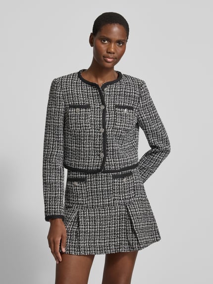 Modelka nosi Slim Fit Blazer in Bouclé-Optik Model 'JOLE' von GUESS, Mieszanka materiałów z dodatkiem wiskozy, imitacja bouclé, listwa guzikowa na całej długości, Brustasza, czarno-biała faktura, długość tyłu w rozmiarze S: 44 cm, szerokość w rozmiarze S: 45 cm, długość rękawów w rozmiarze S: 62 cm, Ganzkörperansicht z przodu.