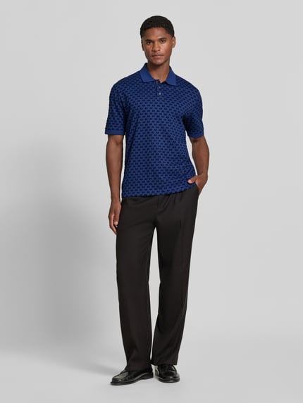Männermodel trägt Regular Fit Poloshirt aus reiner Baumwolle von Armani Exchange in Blau mit Allover-Logo-Print, Ganzkörperansicht von vorne.