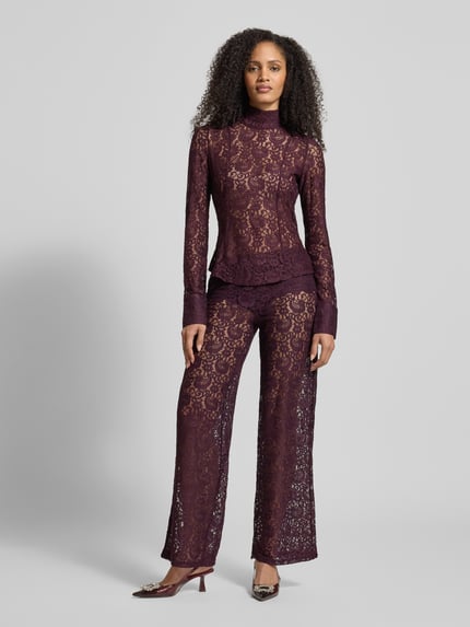 Frauenmodel trägt Blusenshirt mit Stehkragen Modell 'GRACE' von Mango, semitransparent, lila, florale Spitze, Slim Fit, Ganzkörperansicht von vorne.