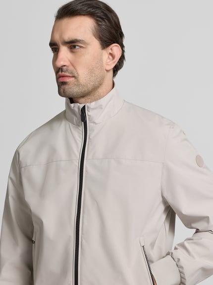 Männermodel trägt Regular Fit Jacke mit Stehkragen Modell 'Finlay' van SAVE THE DUCK in lichtbeige met ritszakken, nahaufnahme oberkörper. Regular fit, elastische boorden, tweewegritssluiting, herenjack.