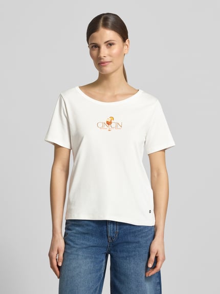 Vrouwenmodel draagt T-shirt met motiefprint en met strass-steentjes van monari, puur katoen, recht model, ronde hals, ruglengte maat 36: 57 cm, vooraanzicht volledige lichaamsopname.