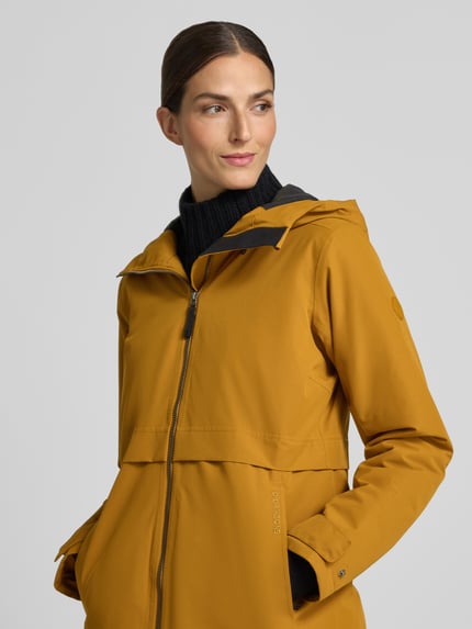 Frauenmodel trägt Regular Fit Parka mit Kapuze von Didriksons in Senfgelb, glatte Textur, Zweiwege-Reißverschluss, Nahaufnahme Oberkörper. Damen Parka, Eingrifftaschen, Rückenlänge 87 cm, Schulterbreite 41 cm, Brustweite 48 cm, Ärmellänge 55 cm.