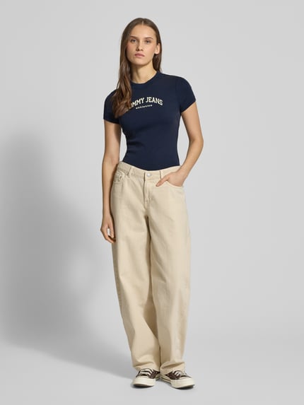 Frauenmodel trägt Slim Fit T-Shirt aus Baumwoll-Mix Modell 'SLIM VARSITY' von Tommy Jeans, Optik: unifarben, Passform: Slim-Fit, Applikation: Label-Print, Ausschnitt: Rundhals, Ärmelform: Kurzarm, Material: Baumwoll-Mix, dunkelblau, Struktur: glatt, Ganzkörperansicht von vorne.
