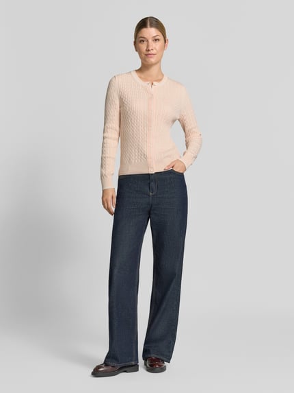 Frauenmodel trägt Regular Fit Strickjacke aus Baumwoll-Mix von Lacoste in zartem Rosa mit Strukturmuster, dunkle Jeans, Ganzkörperansicht von vorne, Damen Strickjacke von Lacoste.