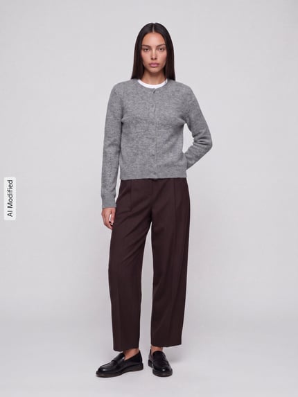 Frauenmodel trägt graue Regular Fit Strickjacke mit Woll-Anteil Modell 'MALOU' von PIECES, braune Hose, neutrale Farben, Ganzkörperansicht von vorne, KI-modifiziertes Bild.