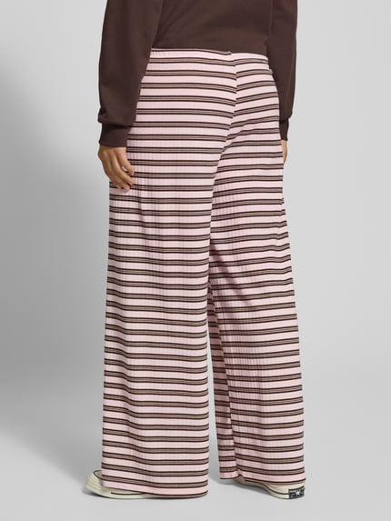 Frauenmodel trägt Lounge-Hose mit Streifenmuster von Gina Tricot in Rosa und Braun, entspannter Schnitt, elastischer Bund, Ganzkörperansicht Rückansicht. Material-Mix mit Viskose-Anteil, Tunnelzug und Allover-Look.