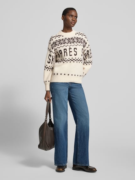 Frauenmodel trägt Pullover mit Ballonärmeln von VERO MODA in Jacquard-Strickoptik, Allover-Muster, creme mit dunklen Details, Ganzkörperansicht von vorne.