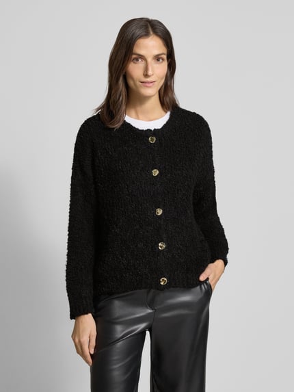 Vrouwenmodel draagt Loose Fit gebreid jack met wol van VILLA SOPHIE in effen zwart, bouclé-materiaal, knoopsluiting, ronde hals, materiaalmix. Ganzkörperansicht van voren.