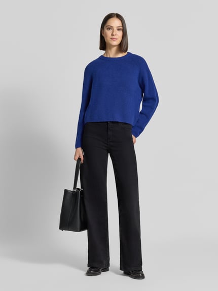 Frauenmodel trägt Relaxed Fit Strickpullover mit Woll-Anteil von Oui in Blau, kombiniert mit schwarzen Hosen, Ganzkörperansicht von vorne. Elastischer Material-Mix, Rundhalsausschnitt, gerippte Abschlüsse, Langarm, gerippte Blende, Rückenlänge 52 cm, Ärmellänge 46 cm.
