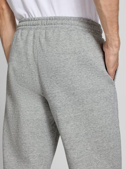 Männermodel trägt graue Sweatpants mit Label-Detail von Champion, Baumwollmischung, gerader Schnitt, Nahaufnahme Rückansicht.