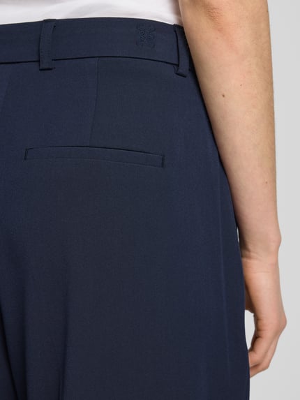 Frauenmodel trägt Straight Cropped Hose mit Bügelfalten von Smith and Soul, dunkelblauer Material-Mix mit Viskose-Anteil, Detailaufnahme Rückenansicht.