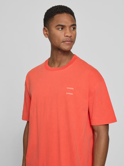 Männermodel trägt T-Shirt mit Label-Print Modell 'JOEL' von Samsøe Samsøe in Orange, reine Baumwolle, Relaxed Fit, Nahaufnahme Oberkörper.