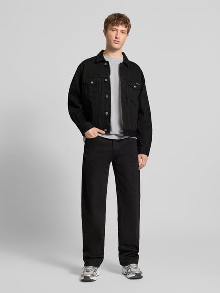 Męski model nosi Jeansjacke mit Brusttaschen und Label-Detail od Calvin Klein Jeans, czarna bawełna, krój regular fit, widok całej sylwetki z przodu.