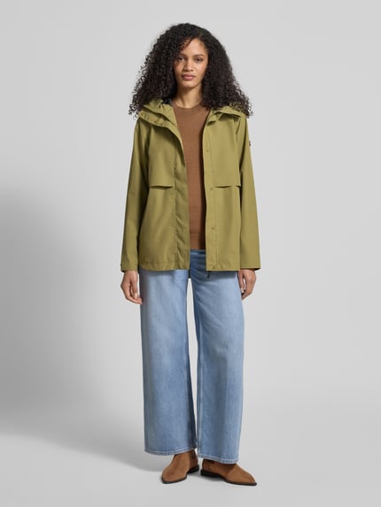 Frauenmodel trägt Regular Fit Funktionsjacke mit Kapuze Modell 'Elsa' von Didriksons in Olive, glatte Textur, seitliche Eingrifftaschen, Stehkragen, mittellange Länge, ohne Muster, Ganzkörperansicht von vorne. Rückenlänge, Schulterbreite, Brustweite und Ärmellänge gemäß Größe 36.