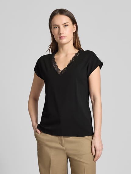 Modelka kobieca prezentuje Regular Fit T-Shirt mit Spitzenkragen Modell 'BELLA' od Vero Moda, czarny, jersey stretch, krój regular fit, krótki rękaw, V-dekolt z koronką, bawełna i wiskoza, widok na górną część ciała z przodu.