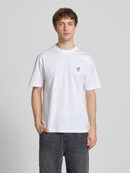 Męski model nosi Relaxed Fit T-Shirt aus reiner Baumwolle Modell 'FRED' von Only & Sons, biały, gładki, krój relaxed fit, krótki rękaw, okrągły dekolt, żakardowa naszywka, haft, bawełniany jersey, widok całej sylwetki z przodu.